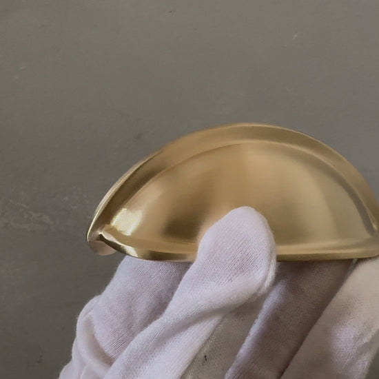 video of one traditional brass cup pull handle on white glove hand